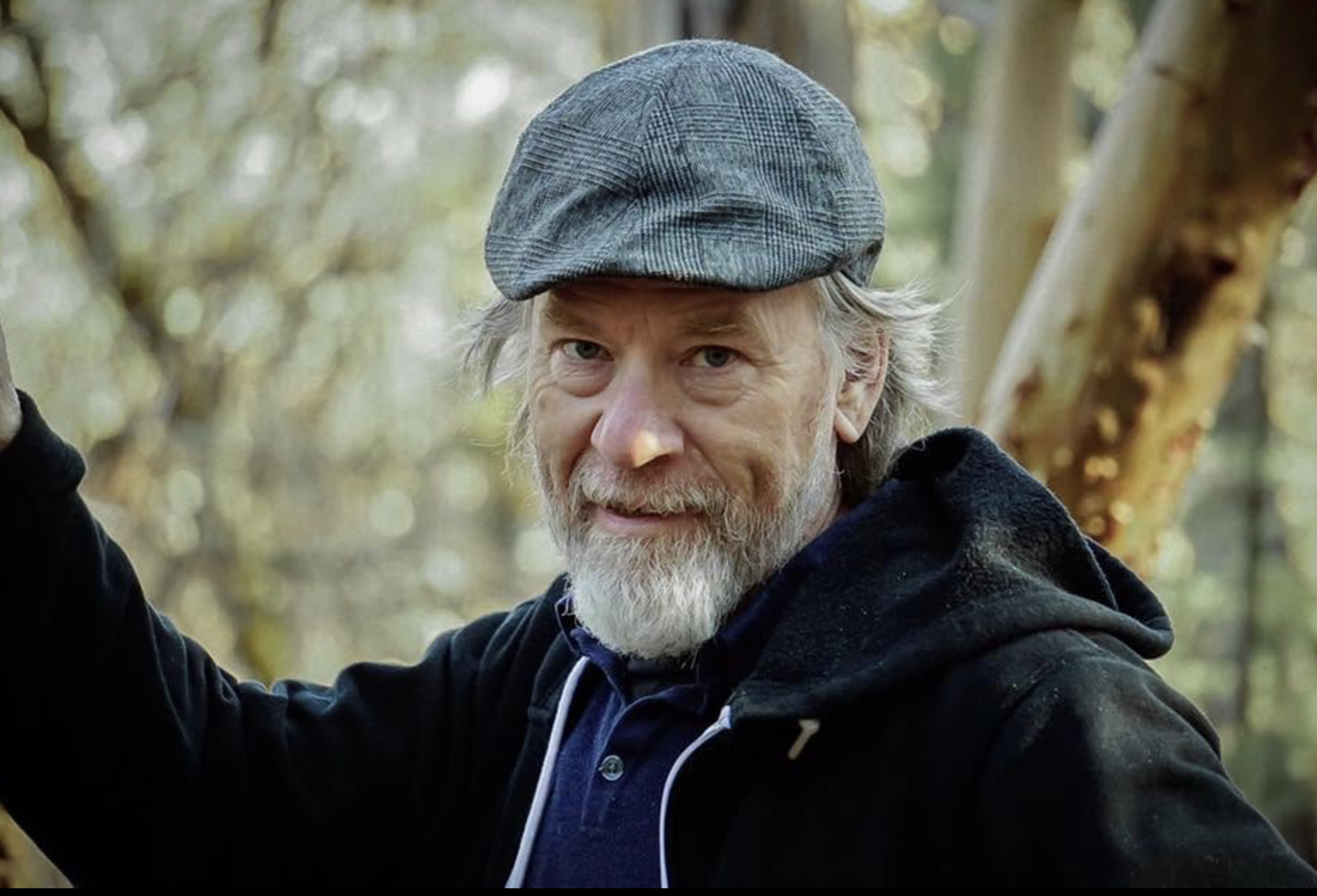 Doug York, in a flat cap and hoodie, leaning against a tree